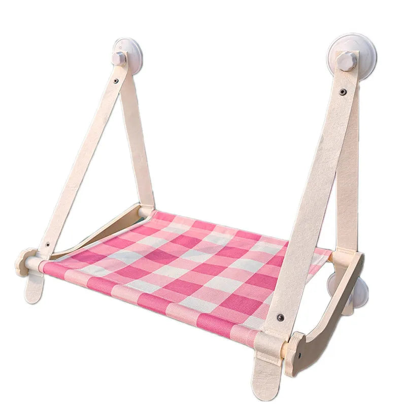 Wooden frame cat hammock with linen mat attached to a window via suction cups, shown in pink colour.