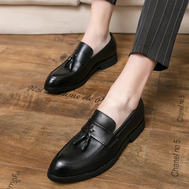 Men's black tassel slip-on loafers with a pointed toe and rubber sole on a white background.