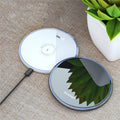 Black Qi fast wireless charging pad on a desk next to a smartphone, showing a blue LED charging indicator light.