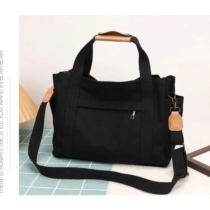 Large horizontal square canvas tote bag with crossbody strap and multiple internal pockets.