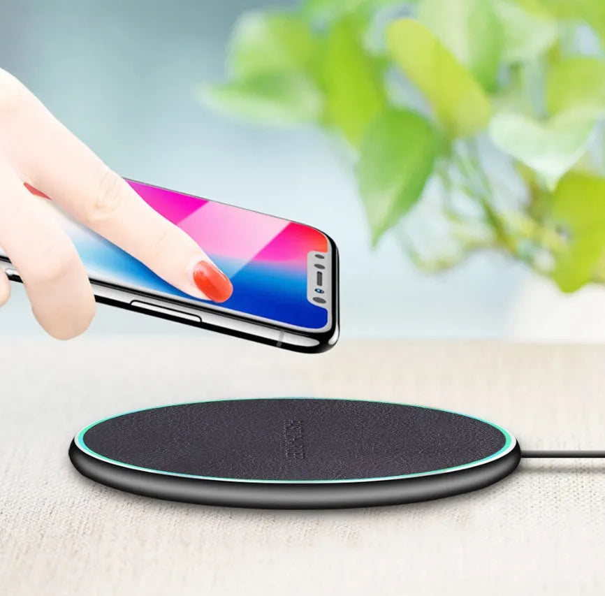 Black Qi wireless charging pad for iPhone 11 on a wooden desk