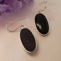 Close-up of women's geometric earrings with oval black agate pendant in silver electroplated setting.