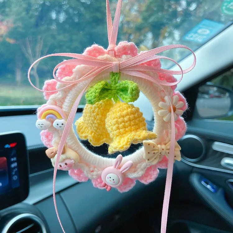 Handwoven wool bell orchid flower car pendant on a green background.