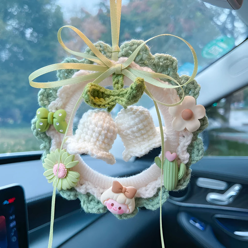 Handwoven wool bell orchid flower car pendant on a green background.
