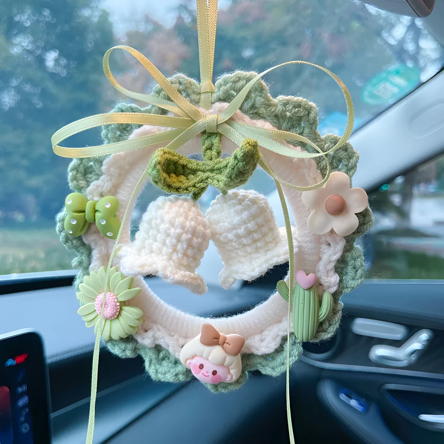 Handwoven wool bell orchid flower car pendant on a green background.
