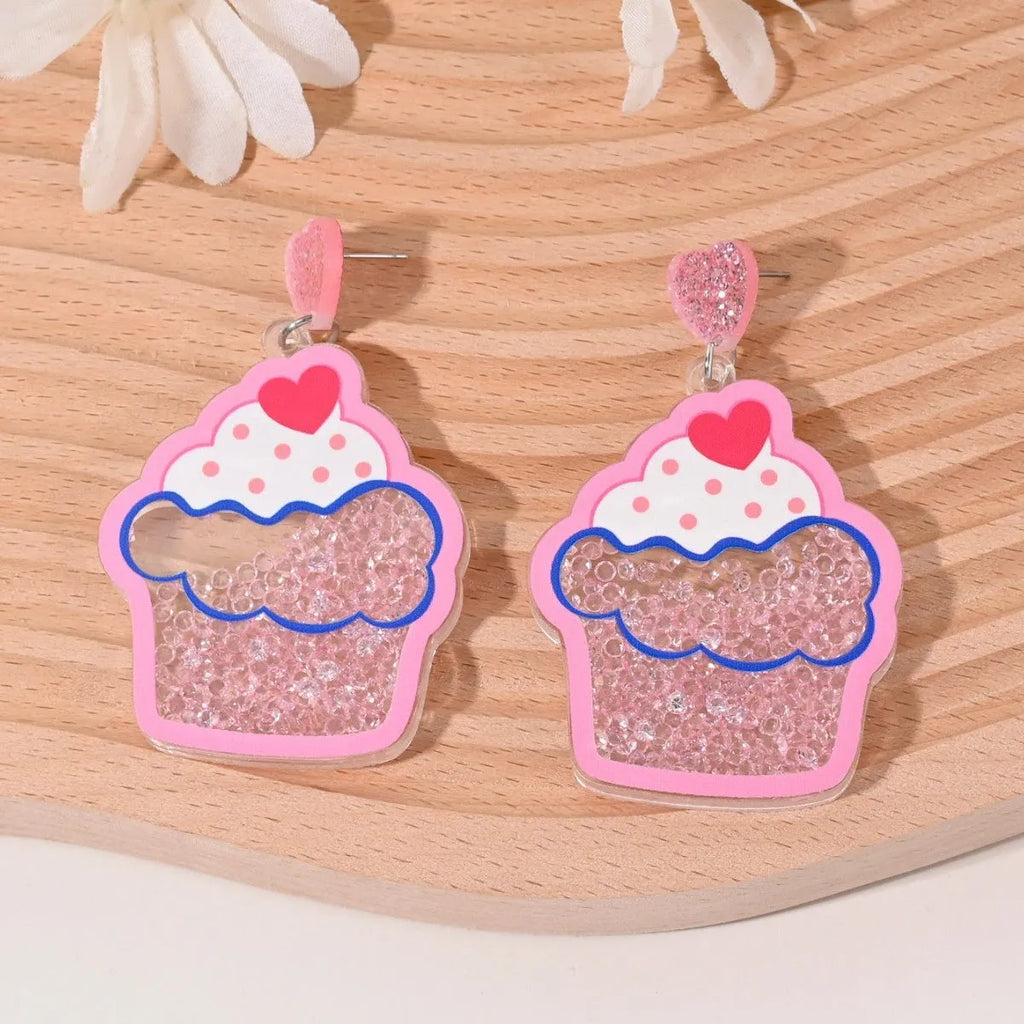 A pair of colourful acrylic earrings with a cake design next to other fruit and ice cream style earrings.