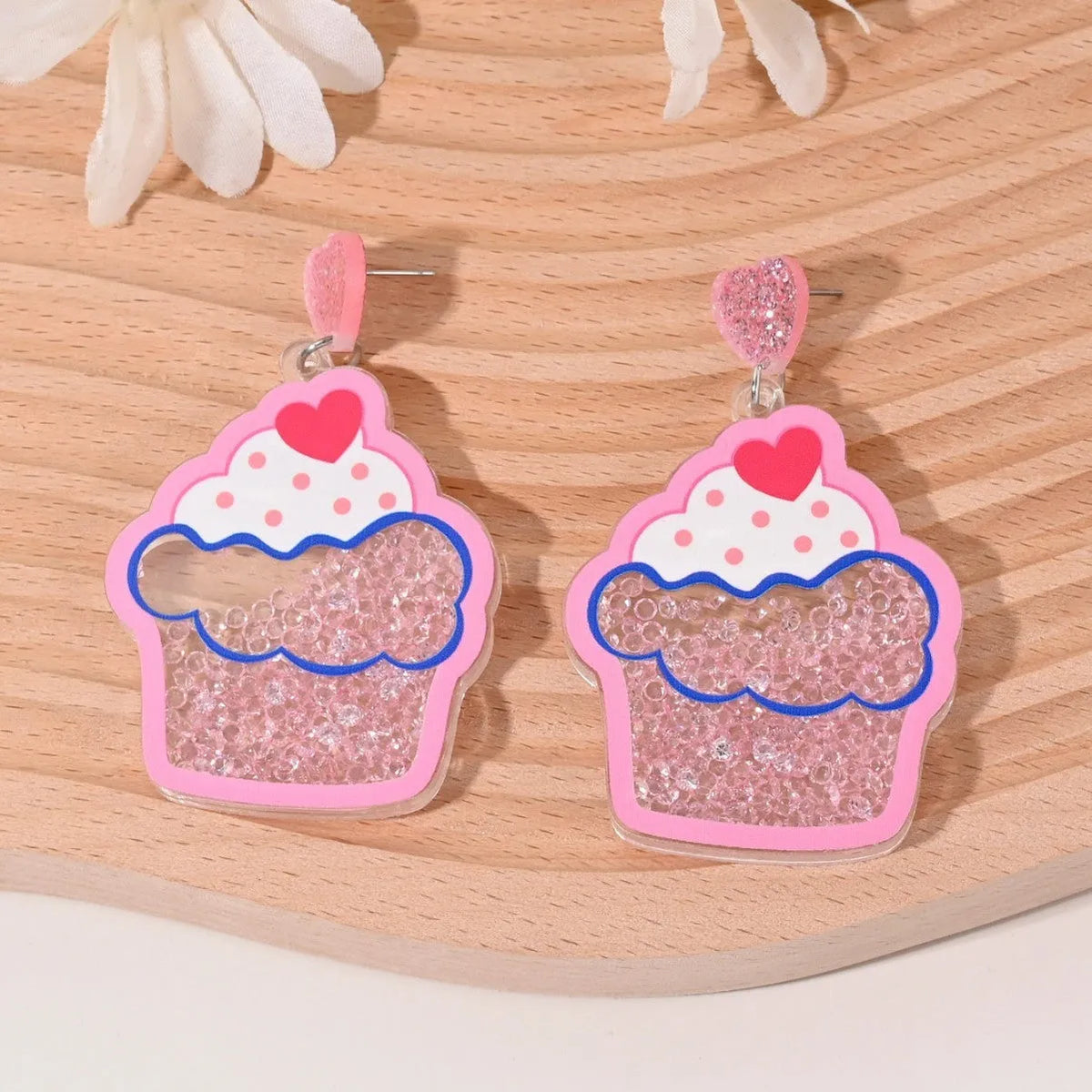 A pair of colourful acrylic earrings with a cake design next to other fruit and ice cream style earrings.