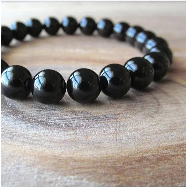 Close-up of a women's black onyx bracelet with 8mm geometric agate beads on a black elastic cord.