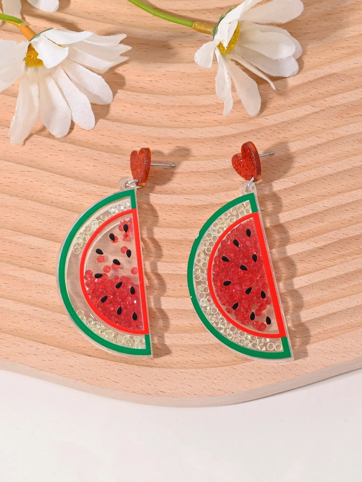 A pair of colourful acrylic earrings with a cake design next to other fruit and ice cream style earrings.