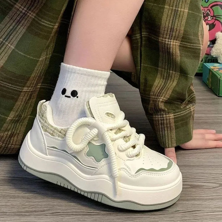 Women's green patent leather platform sneaker with round toe and white rubber sole on a pink background.