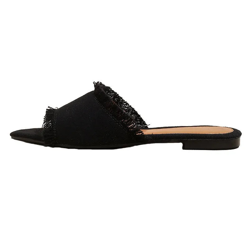 Women's apricot denim flat slippers with tassel detail on a grey background.