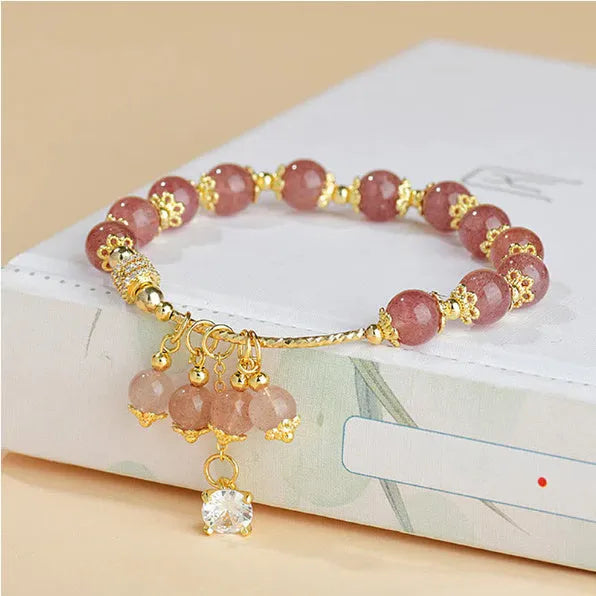 Close-up of a women's pink bracelet with a heart-shaped strawberry quartz crystal and small pearl accents on the band.