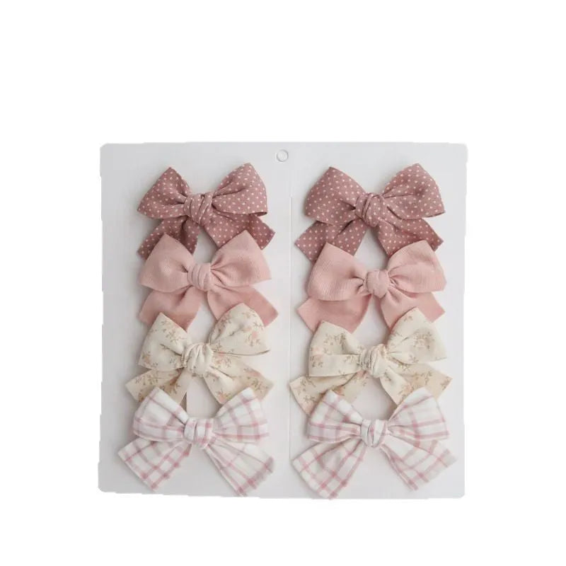 Set of eight children's cloth bow hair clips in various colours including beige polka dot, pink, blue floral, and wine red plaid patterns.