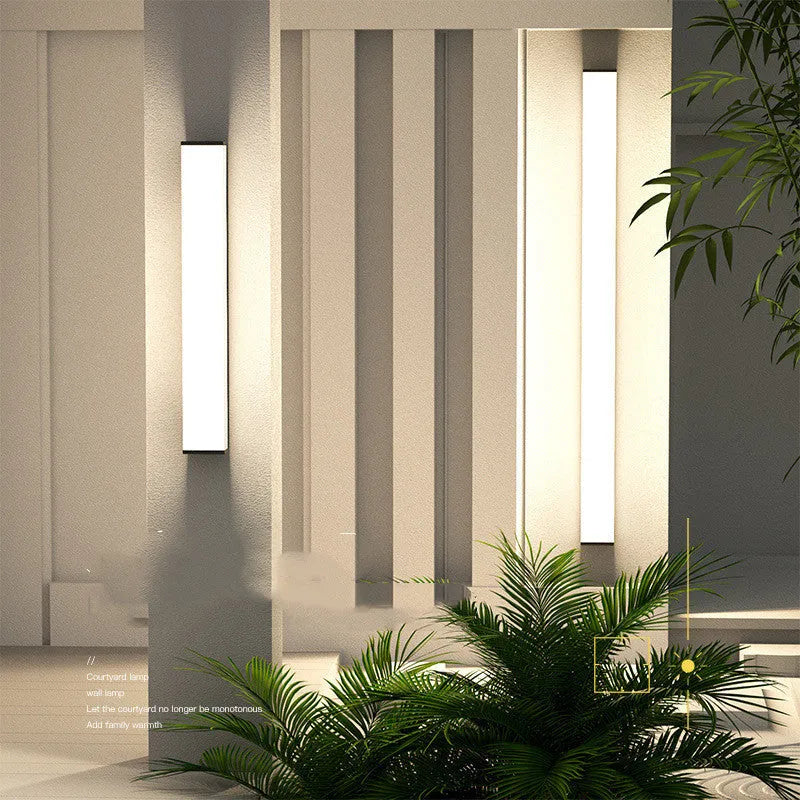 Long, slim stainless steel and plastic outdoor wall light mounted on a brick wall.