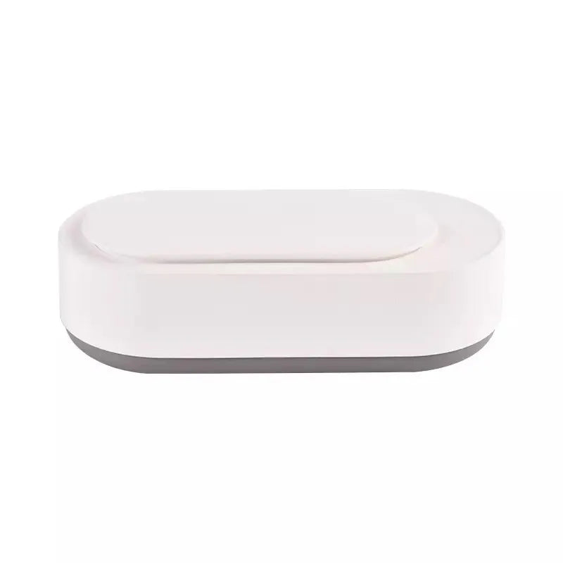 White portable ultrasonic cleaner with touch button next to jewellery and glasses on a table.