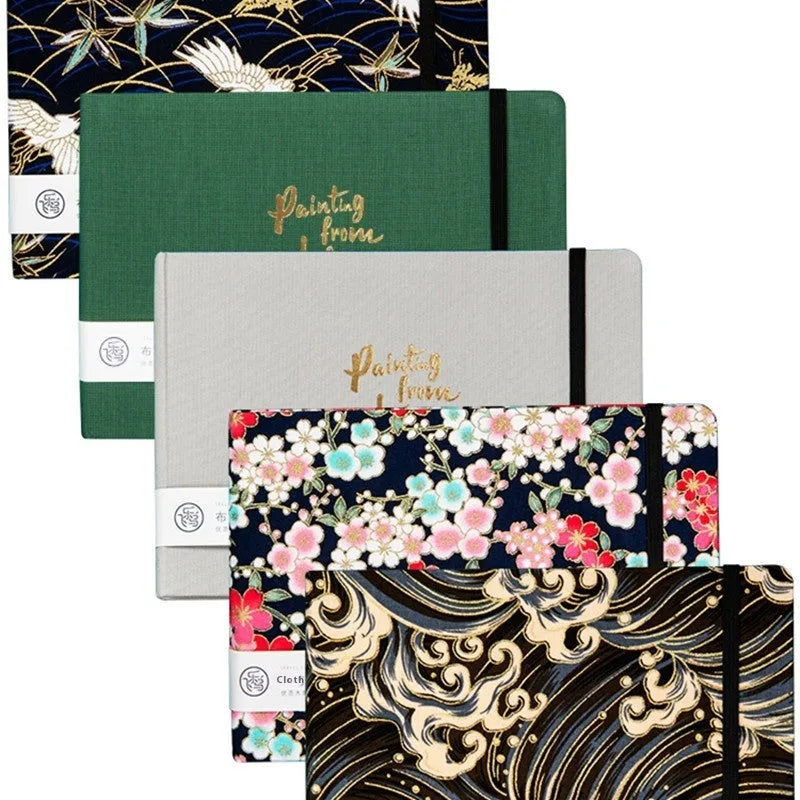 Feiluniao fabric-covered watercolour notebook open on a table with art supplies.