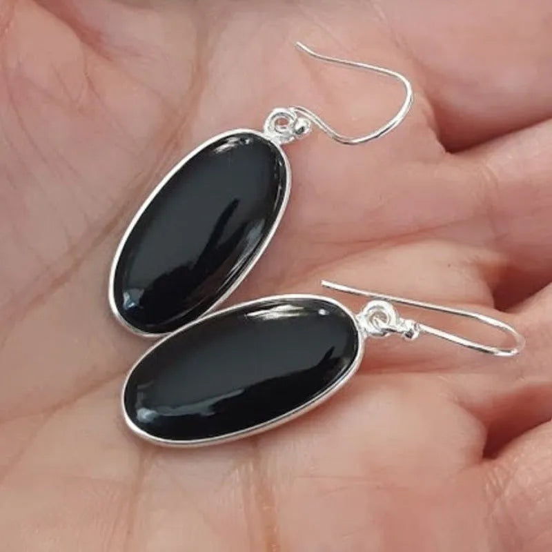 Close-up of women's geometric earrings with oval black agate pendant in silver electroplated setting.