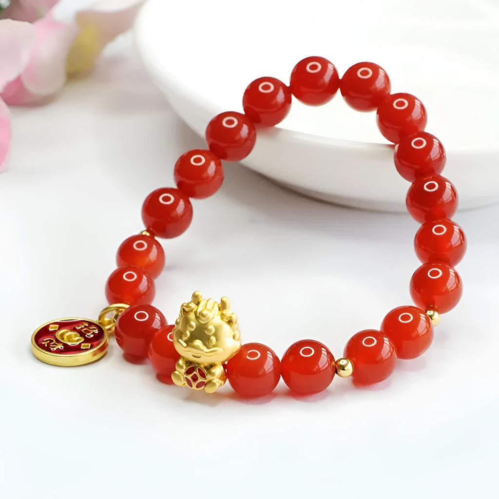Close-up of a red agate beaded bracelet with a dragon zodiac charm on a wrist.