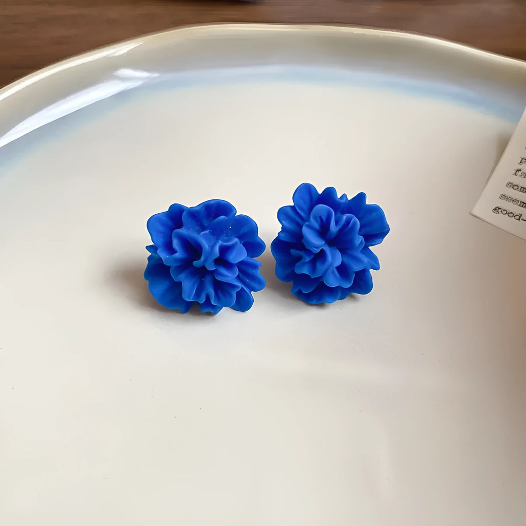 Women's geometric earrings with blue resin flower and silver needle on cloth background