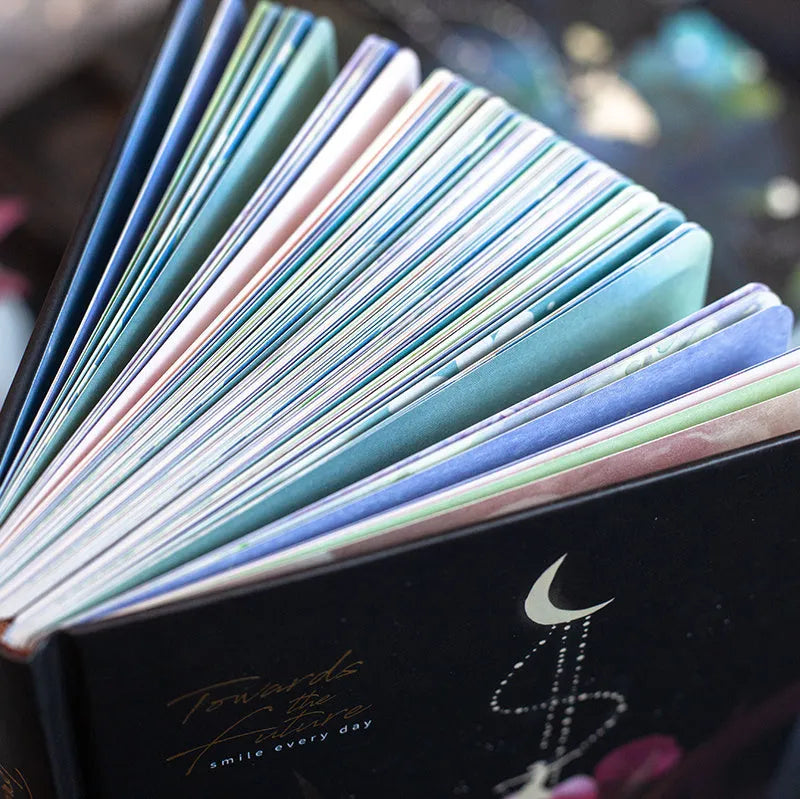A5 notebook with luminous holographic cover lying flat, showing colourful illustrated interior pages.
