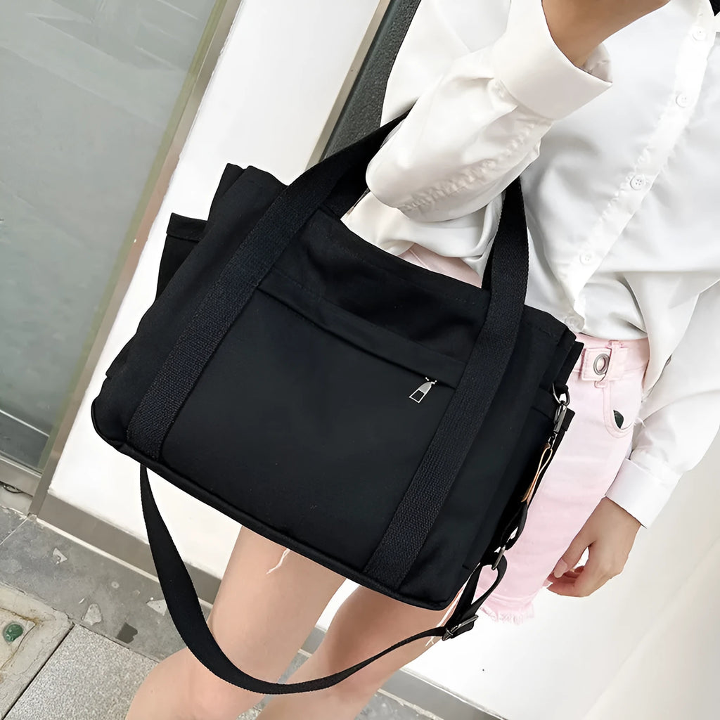 Large horizontal square canvas tote bag with crossbody strap and multiple internal pockets.