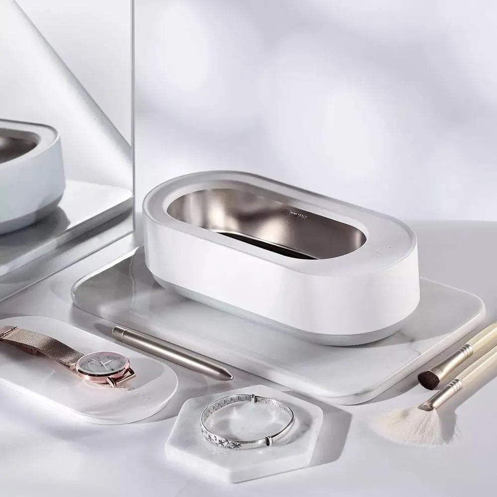 White portable ultrasonic cleaner with touch button next to jewellery and glasses on a table.