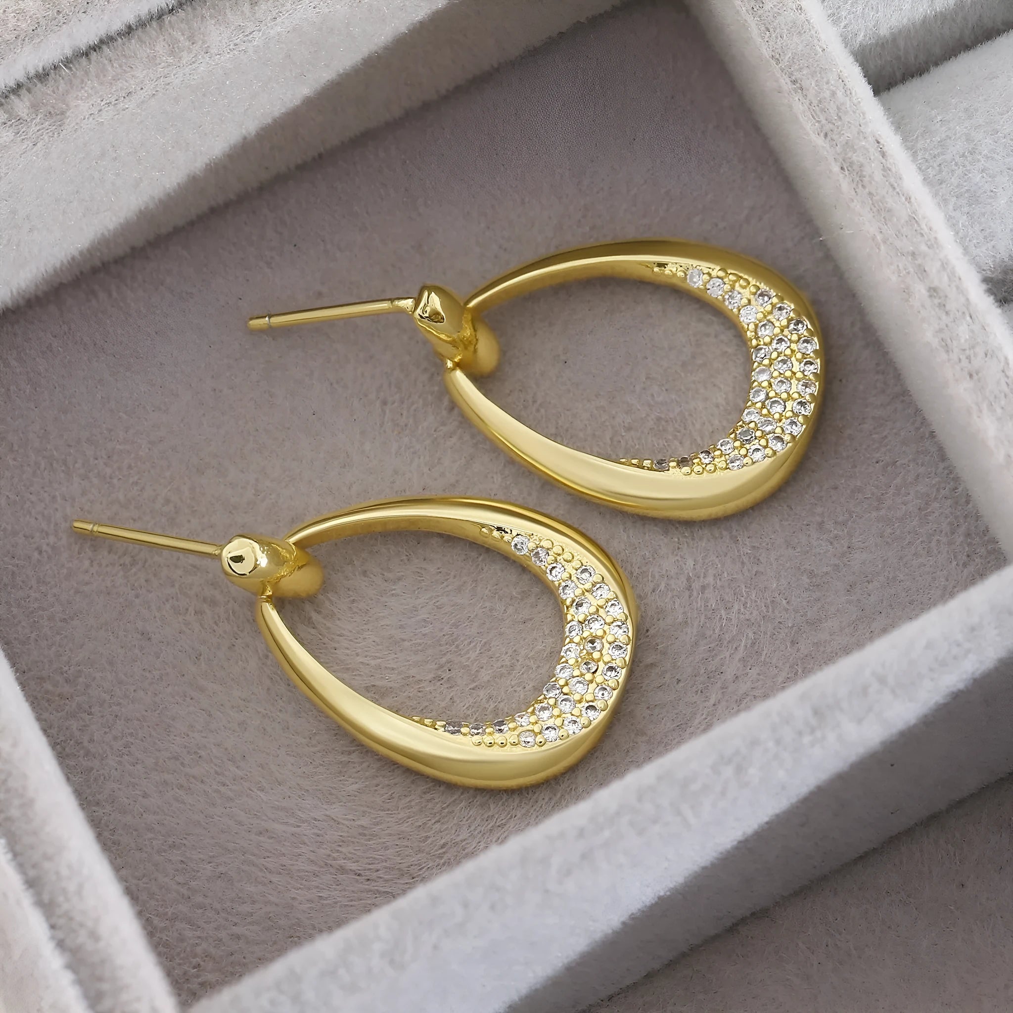 Yellow gold geometric drop earrings with round and oval ring elements on white background