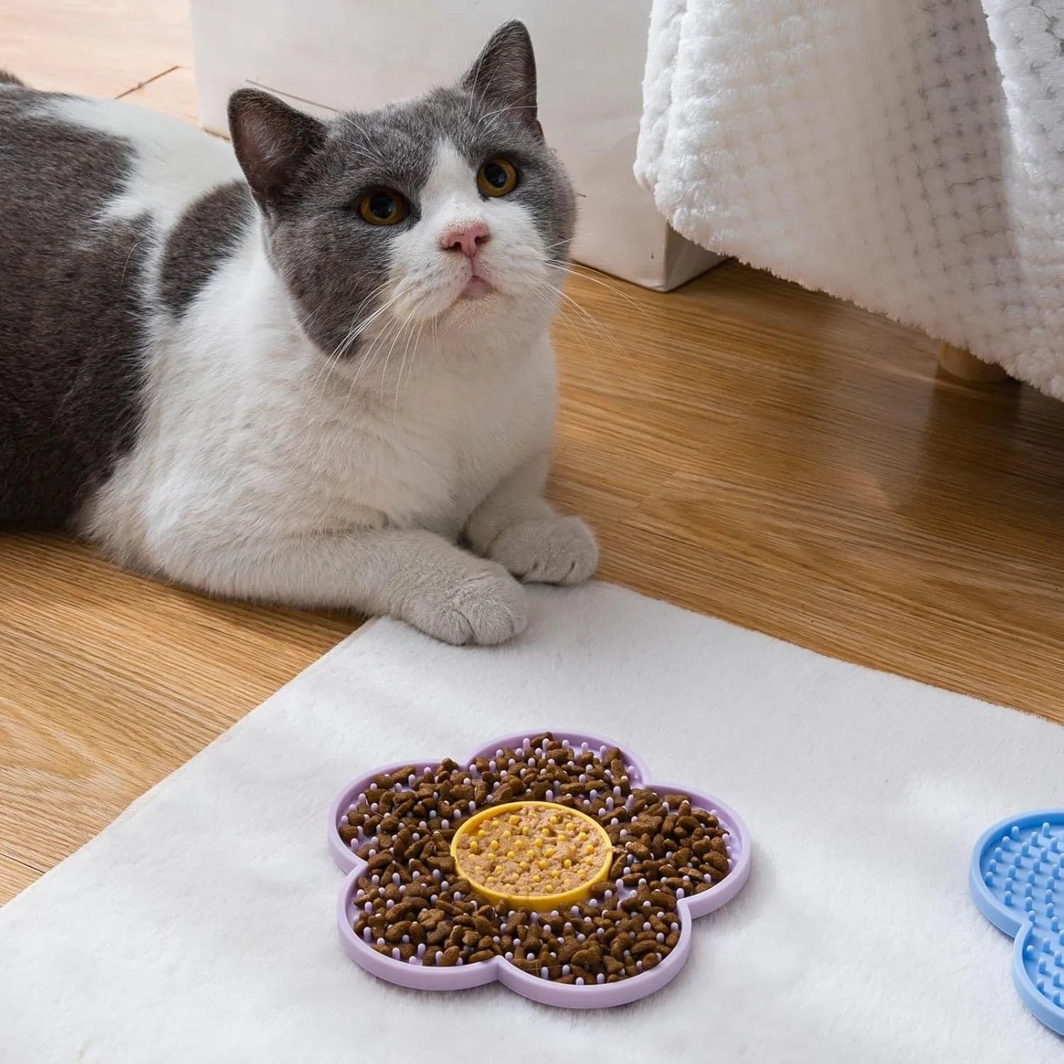 Flower-shaped silicone pet licking mat in blue with suction cups on the back, shown on a tiled surface.