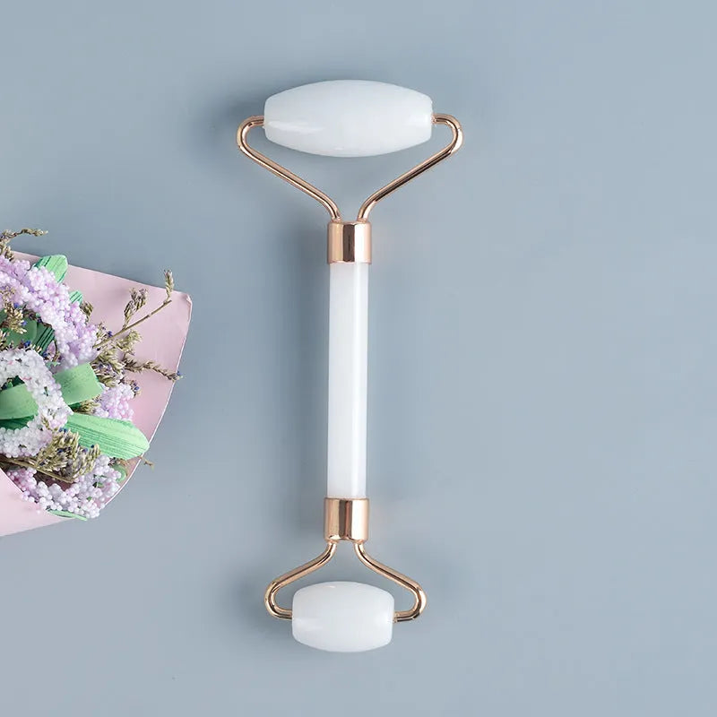 White jade facial roller and gua sha scraper board set on a plain surface.
