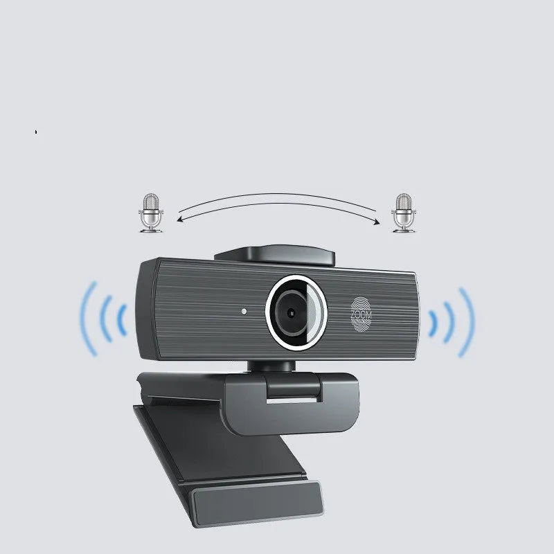 Black USB webcam with magnetic privacy cover on a desk next to a laptop