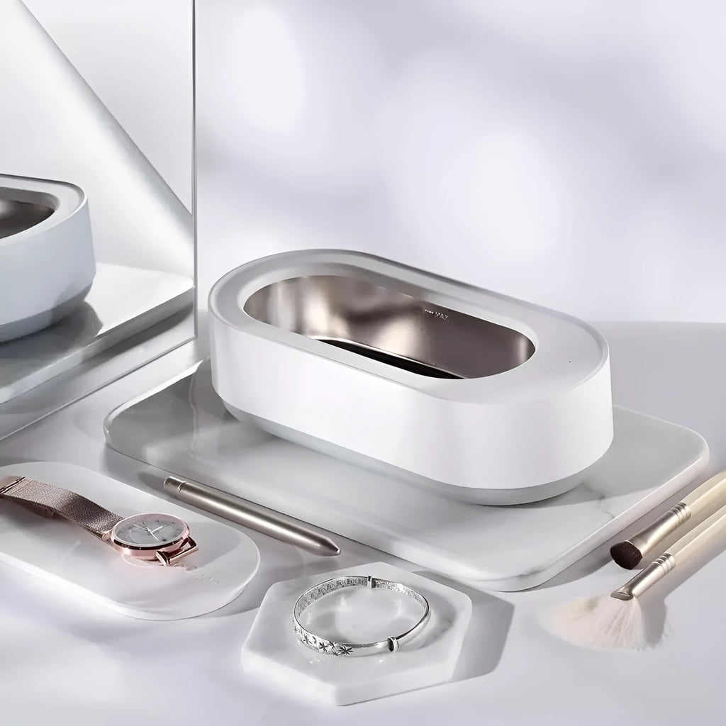White portable ultrasonic cleaner with touch button next to jewellery and glasses on a table.