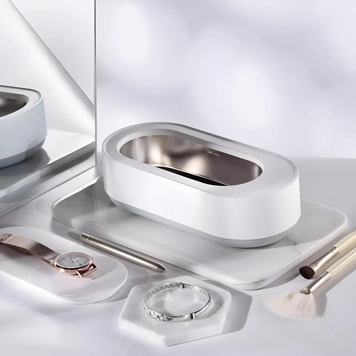 White portable ultrasonic cleaner with touch button next to jewellery and glasses on a table.