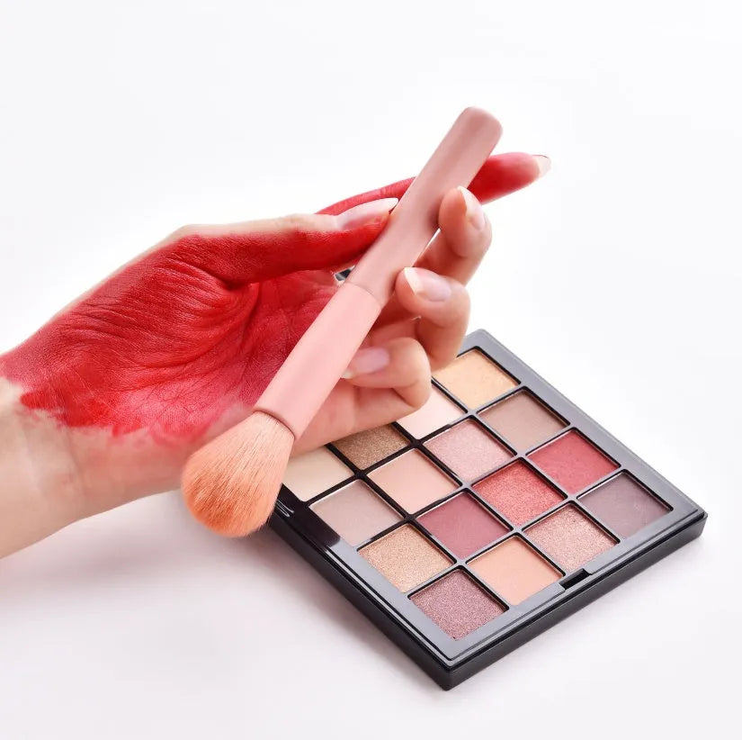 Ten wooden-handle make-up brushes for face and eye application in a pink travel case.