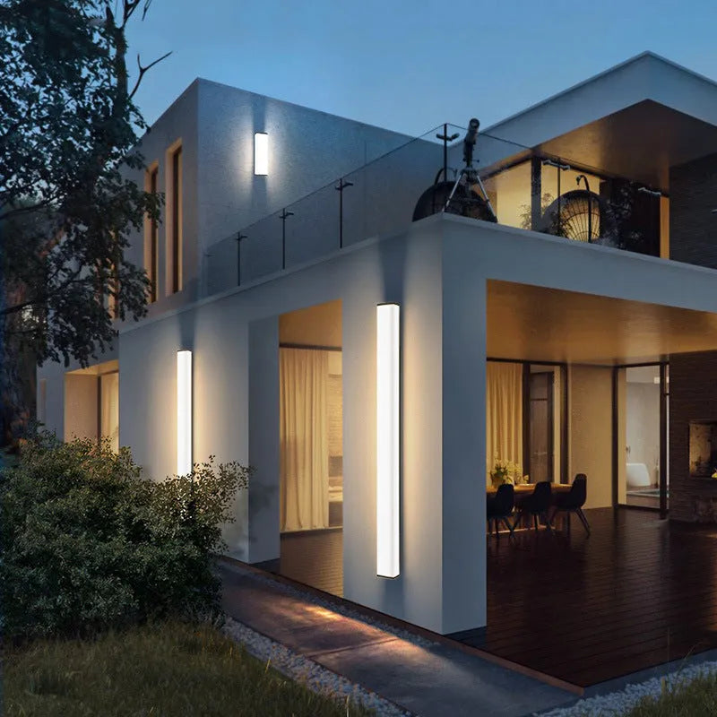 Long, slim stainless steel and plastic outdoor wall light mounted on a brick wall.