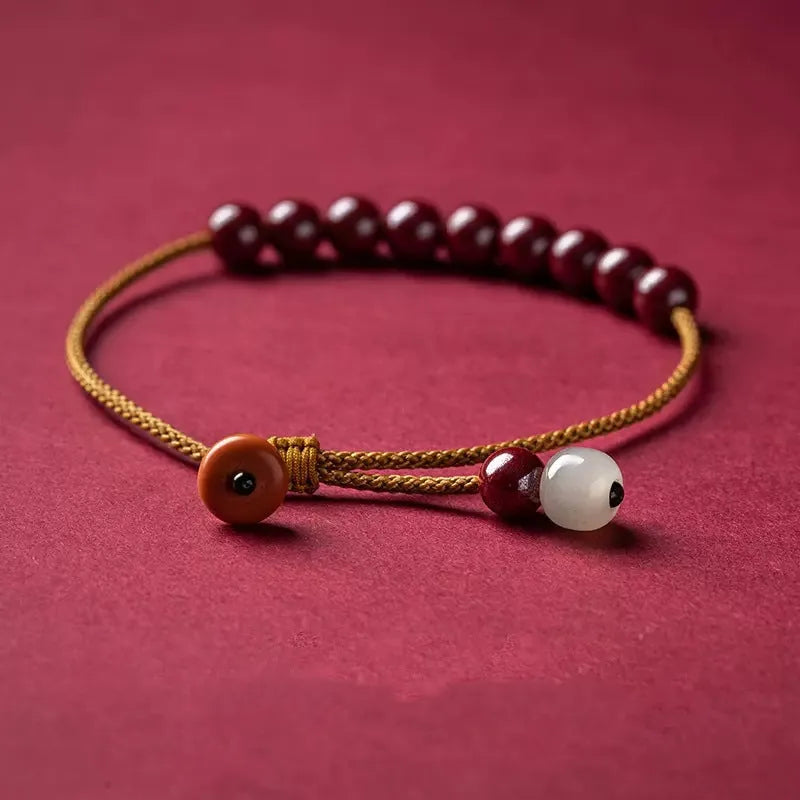 Close-up of a geometric design bracelet made from dark red cinnabar and Hetian jade on a wrist.