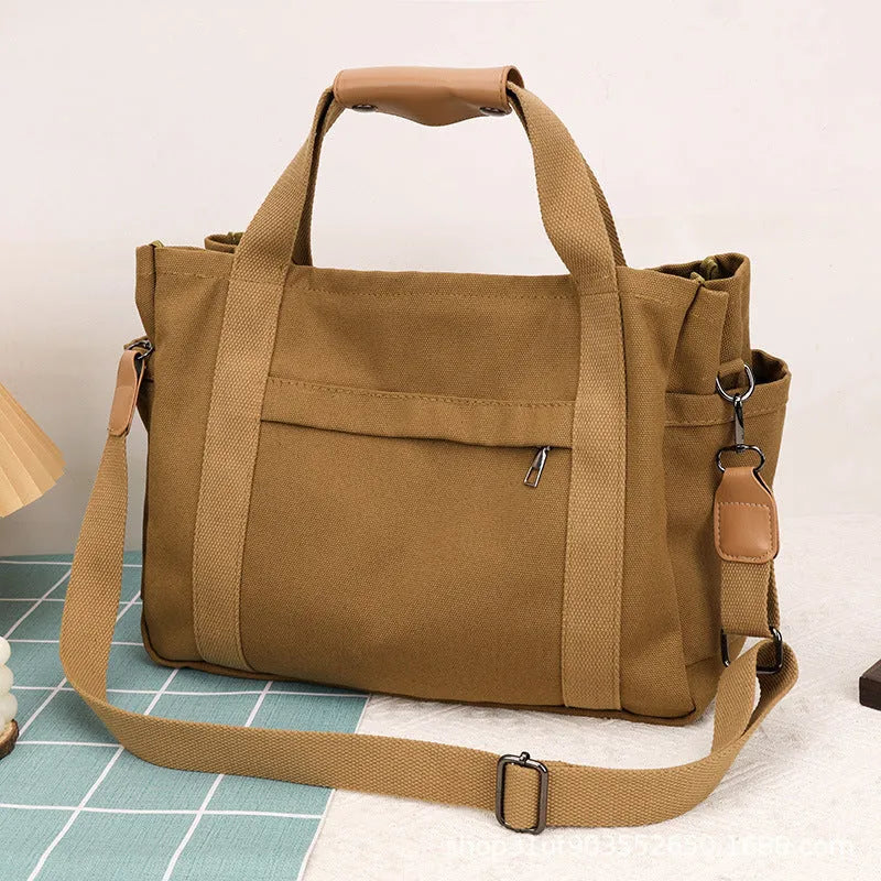 Large horizontal square canvas tote bag with crossbody strap and multiple internal pockets.