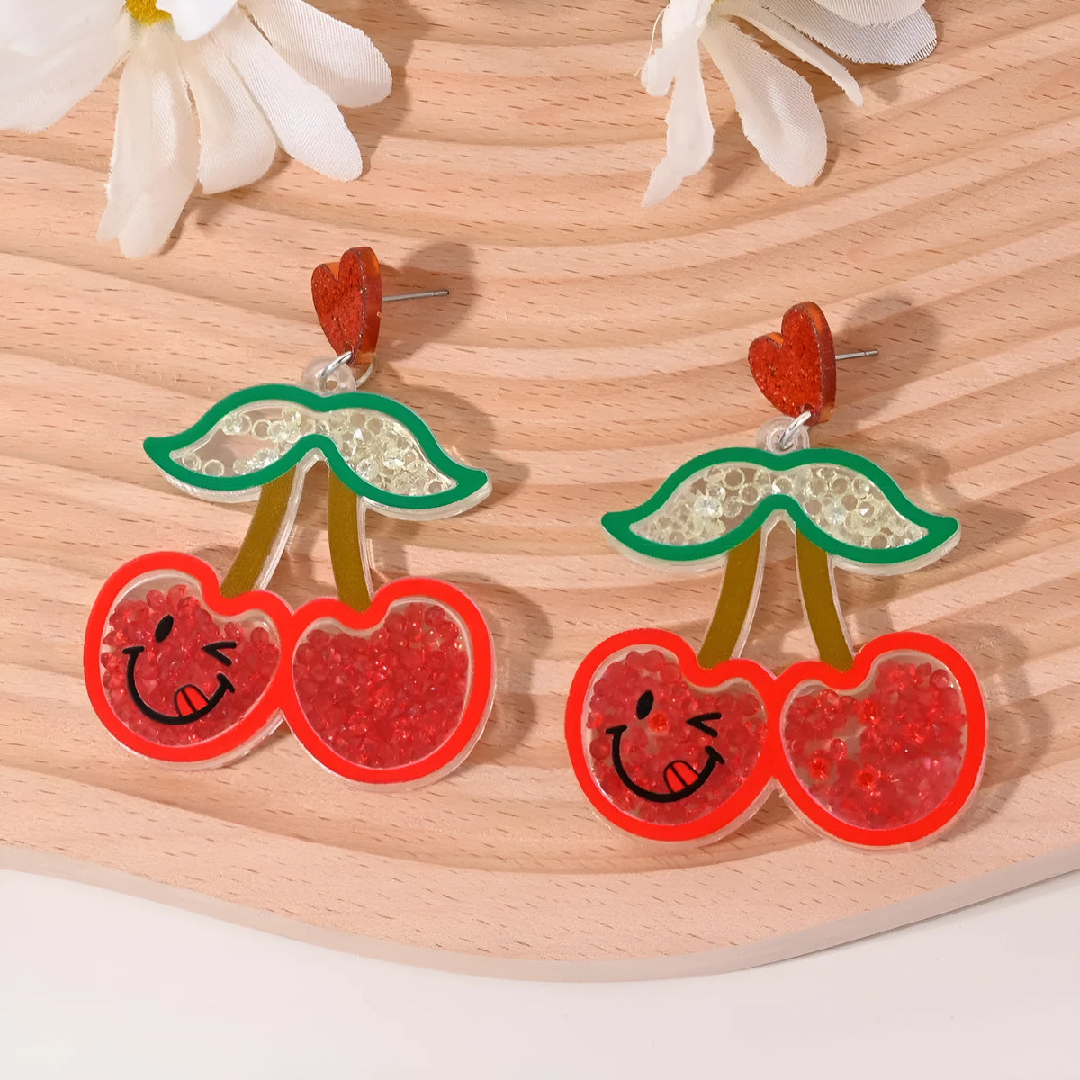 A pair of colourful acrylic earrings with a cake design next to other fruit and ice cream style earrings.