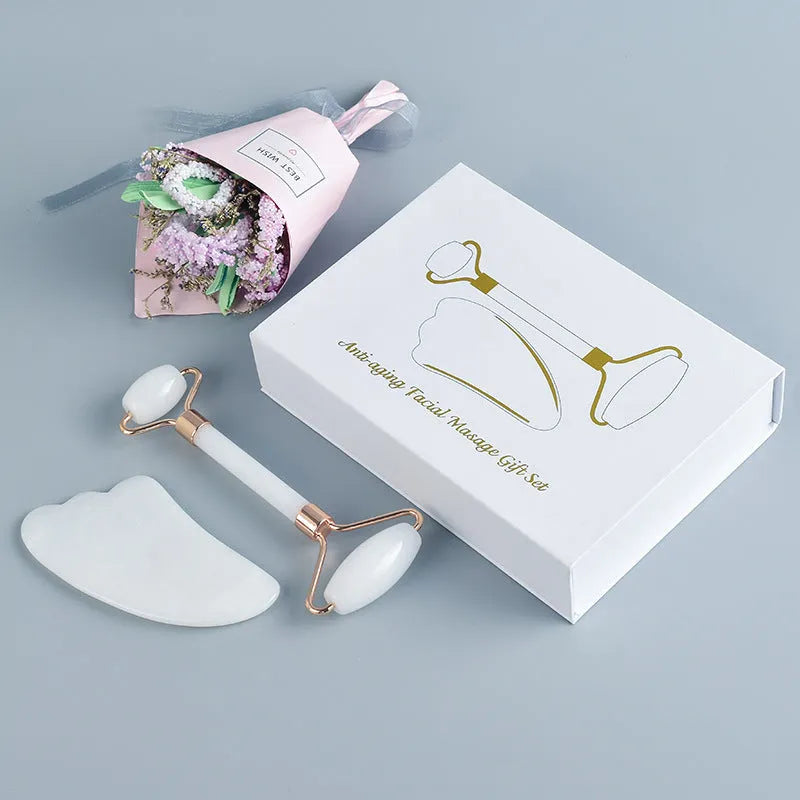 White jade facial roller and gua sha scraper board set on a plain surface.