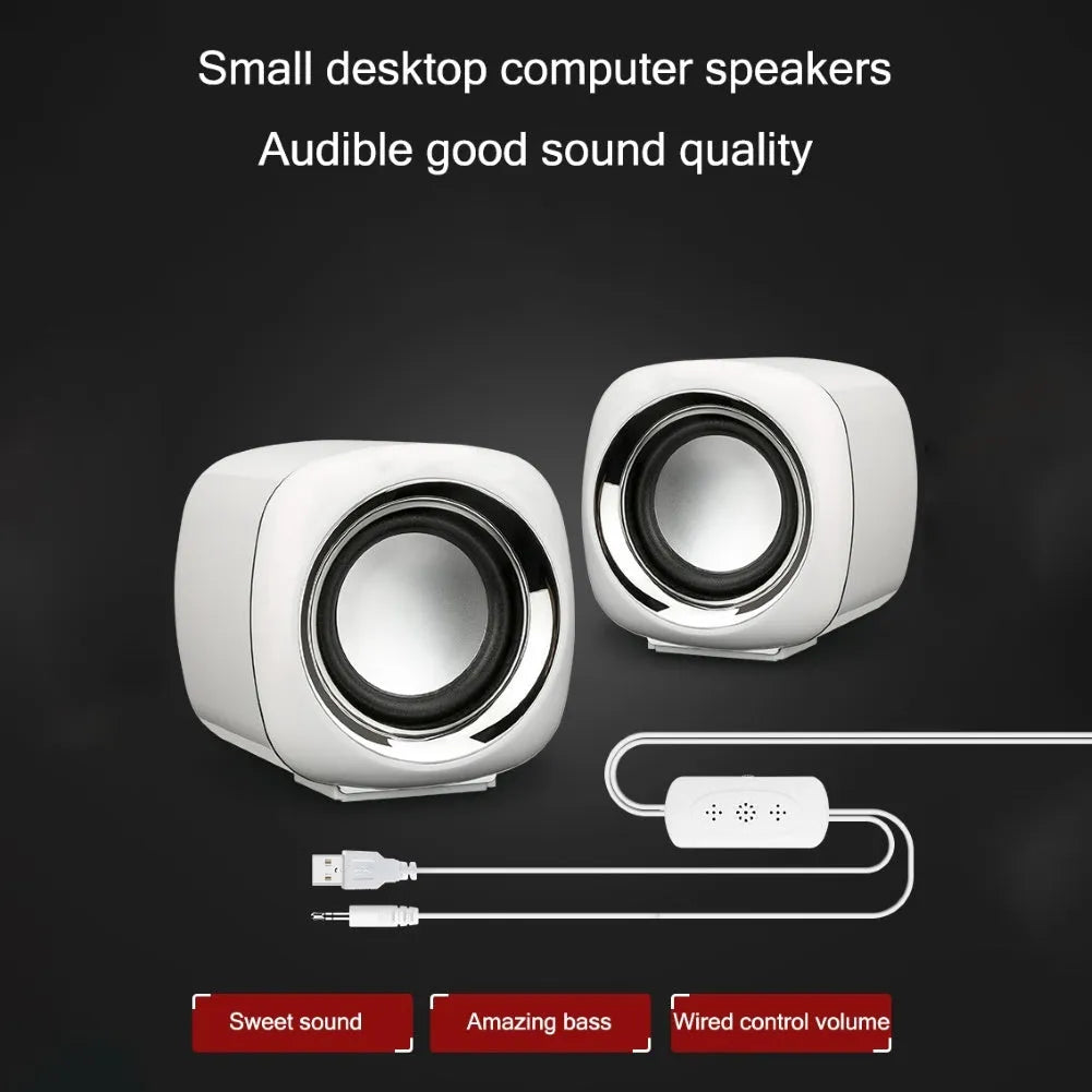 A pair of small black wired computer speakers on a desktop next to a laptop.