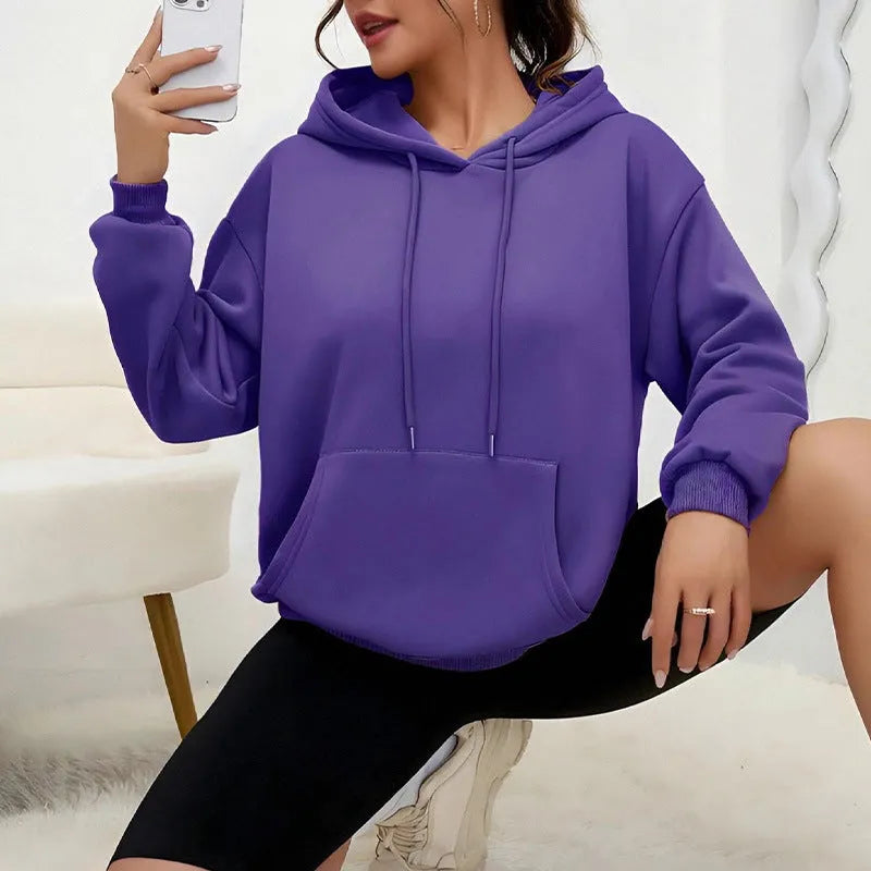 Woman wearing a loose grey sweatshirt with a front pocket and drawstring hem.