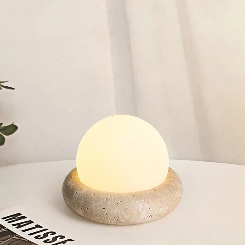 Cream coloured spherical bedside night lamp with remote control on wooden table