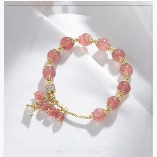 Close-up of a women's pink bracelet with a heart-shaped strawberry quartz crystal and small pearl accents on the band.