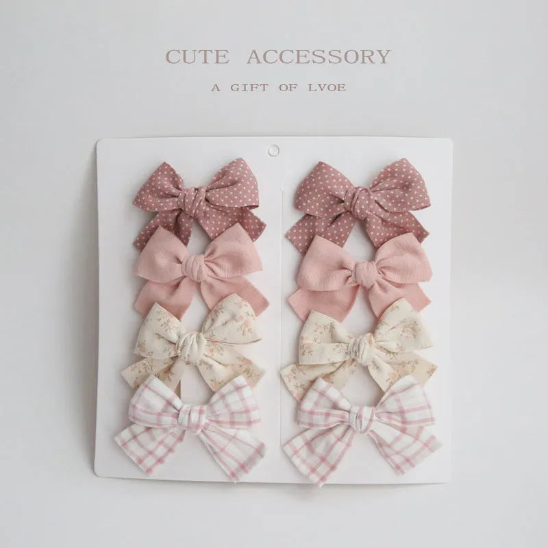 Set of eight children's cloth bow hair clips in various colours including beige polka dot, pink, blue floral, and wine red plaid patterns.
