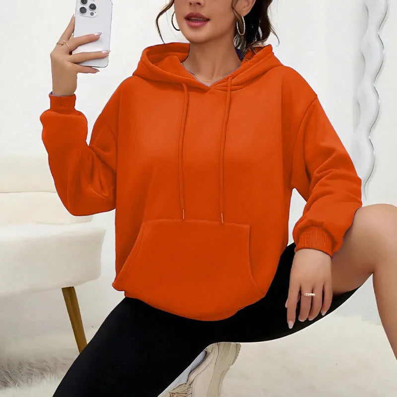 Woman wearing a loose grey sweatshirt with a front pocket and drawstring hem.