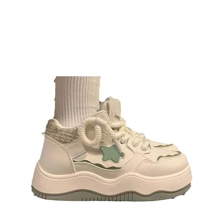 Women's green patent leather platform sneaker with round toe and white rubber sole on a pink background.