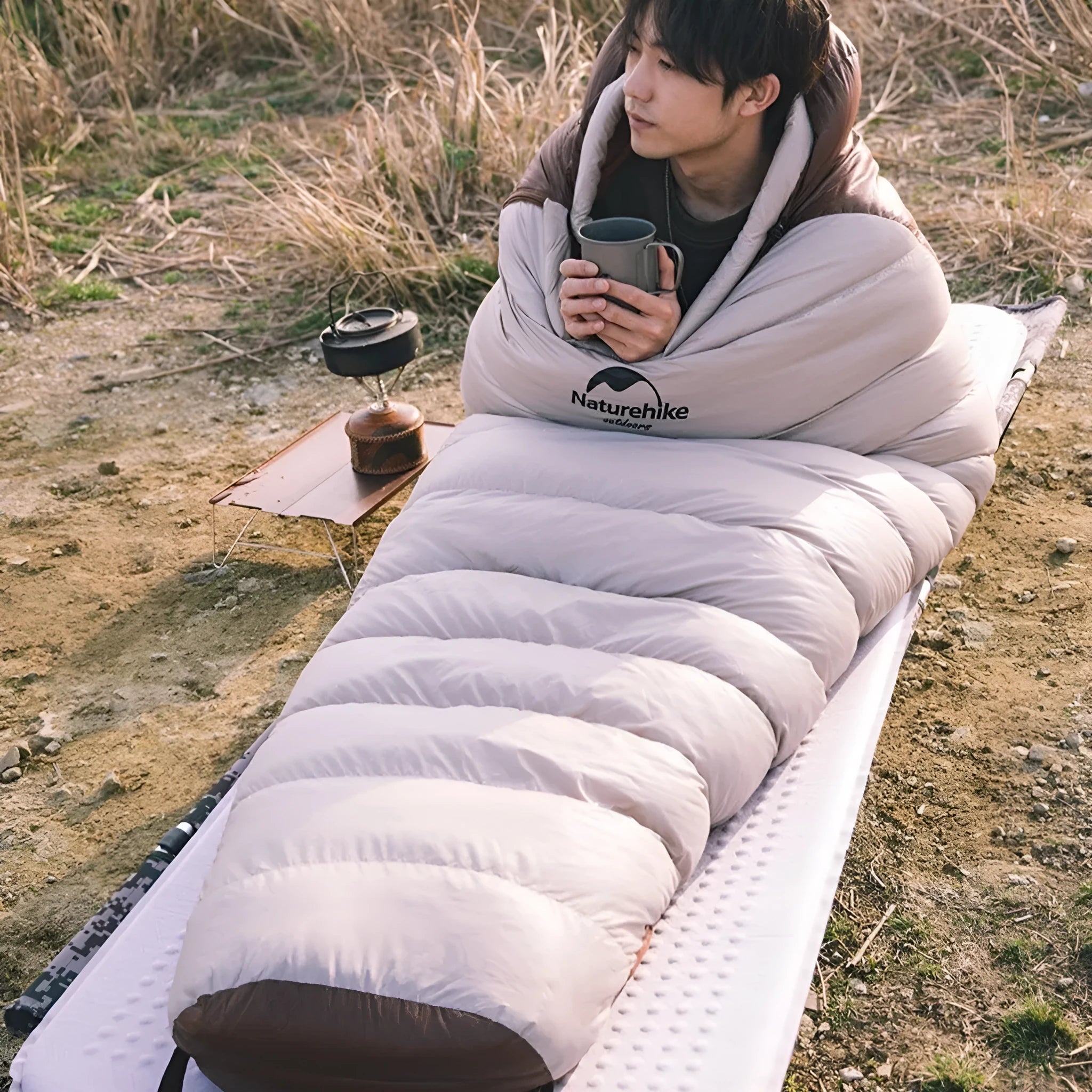 Blue and grey mummy-style sleeping bag with compression sack on a pine forest floor.
