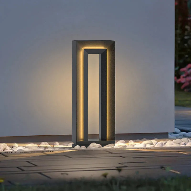 Modern square stainless steel outdoor garden lamp with geometric design on a patio.