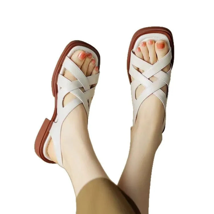 Women's black patent leather beach sandals with square toe and cross-strap design on a light background.