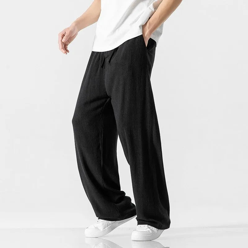 Men's beige linen-style trousers with a loose straight-leg fit and drawstring waist, laid flat.