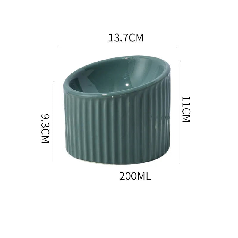 Dark green ceramic elevated cat bowl on a table, showing its raised height and round, tilted shape.